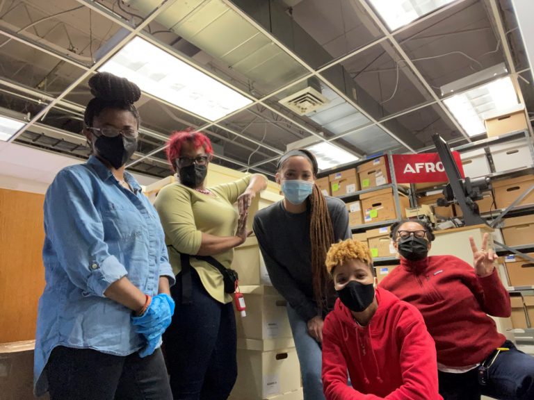 5 women from the Community Archives team in front of several shelves