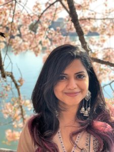 Head shot of HCIM alum Kaush Ganesh in front of cherry blossom trees.