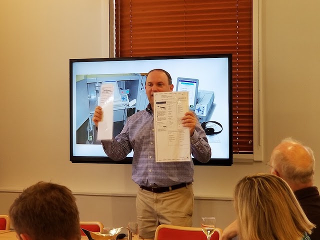 Dr.Lazar standing in front of a tv holding up two long pieces of paper