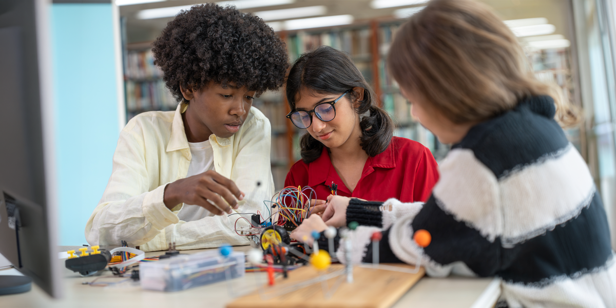 Diverse group of young student teenagers building robot kit together in school library. Multiethnic kids learning stem electronics engineering and robotics technology project